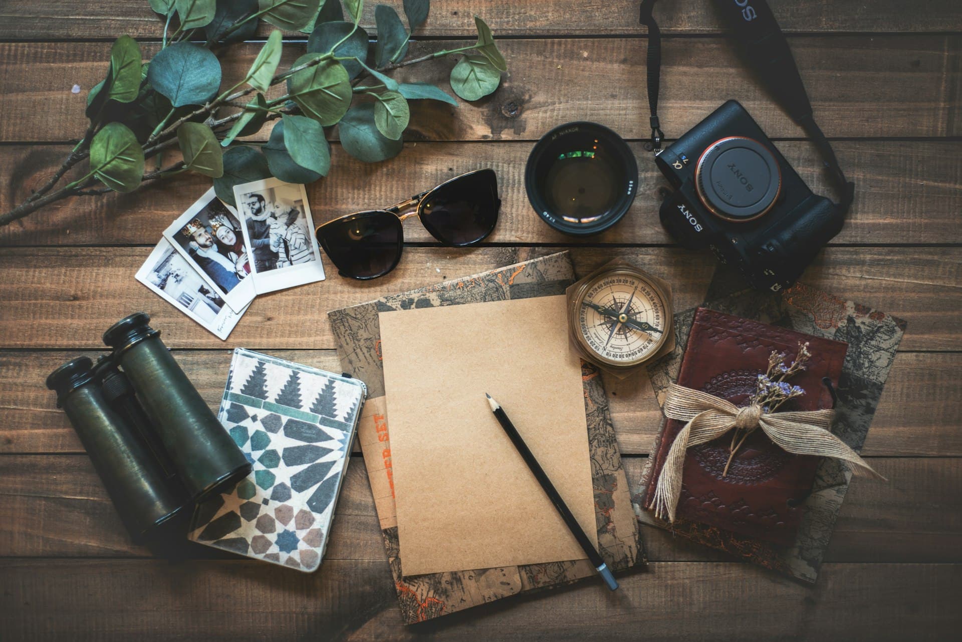 Travel planning essentials — camera, compass, and journal laid out on a wooden table