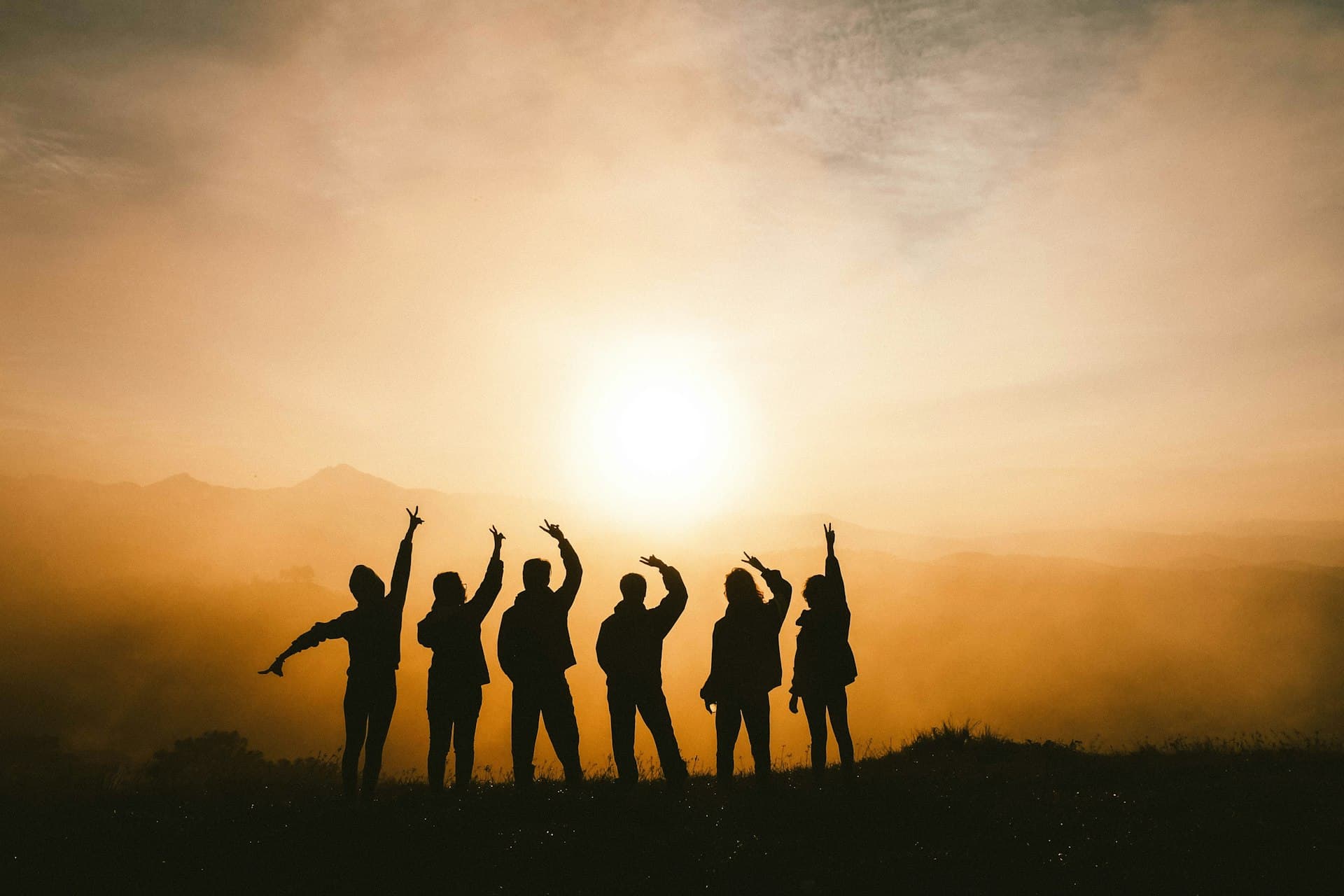A group of friends celebrating together on a mountaintop at sunset