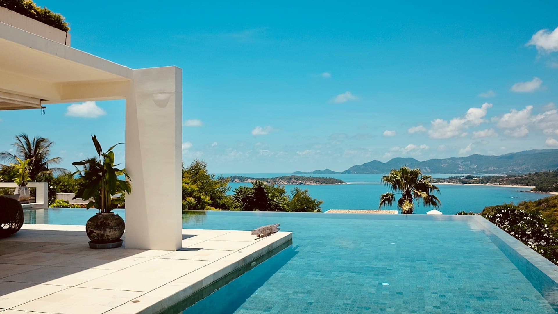 An infinity pool overlooking a blue bay from a villa terrace