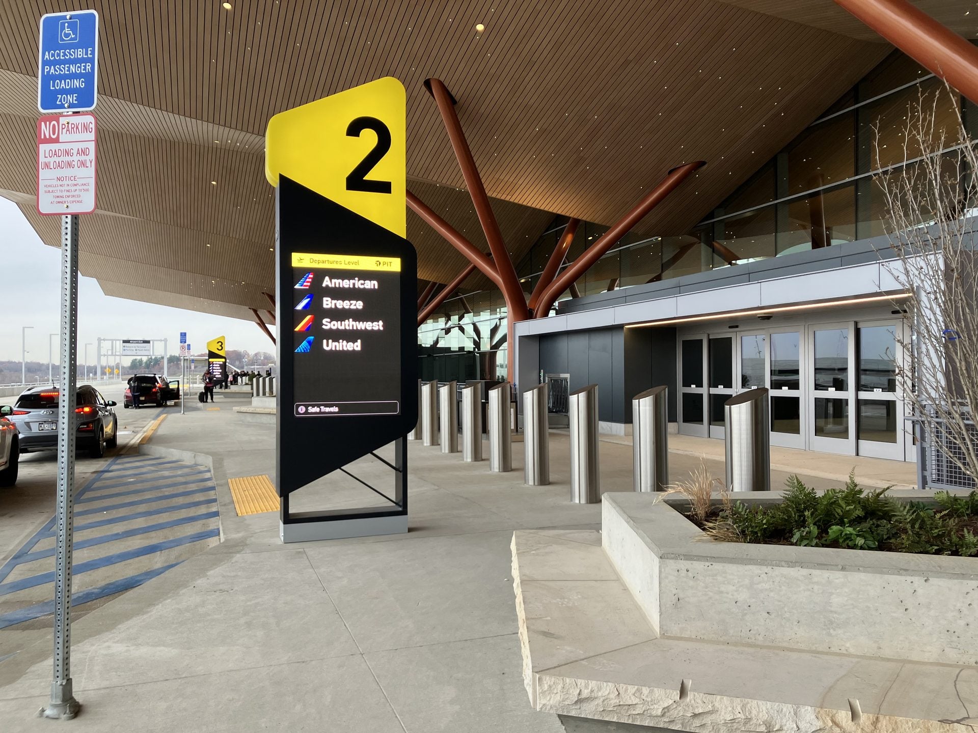 The passenger drop-off zone outside an airport terminal, with cars at the curb